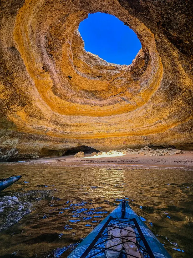 First-person vertical view from inside a kayak looking at the Benagil Cave skylight with golden light illuminating the cave walls