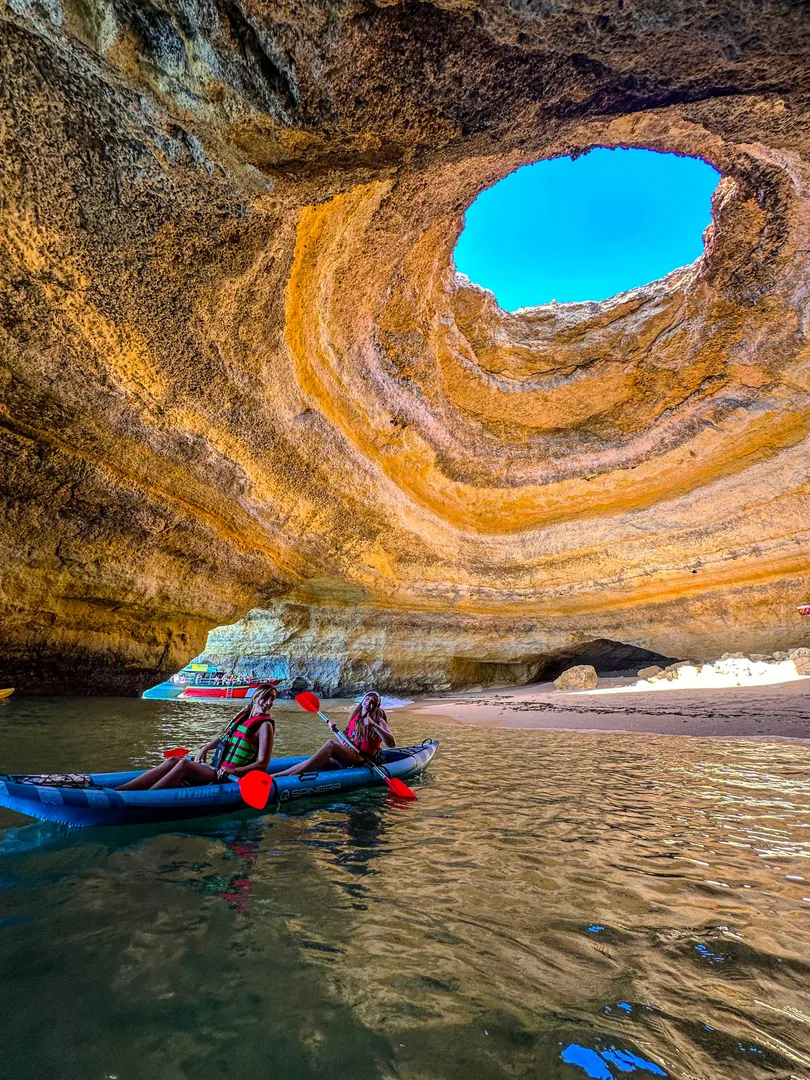 Kayakers paddling below the Benagil Cave skylight with sunlight streaming through the circular opening onto the cave floor