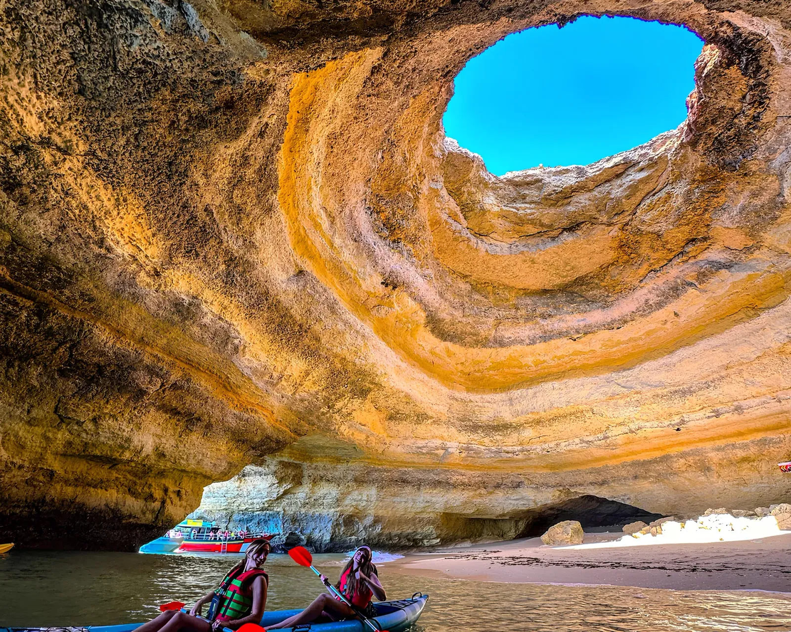 Looking up at the Benagil Cave skylight from a kayak on the water inside the cave, showing the circular opening and blue sky above