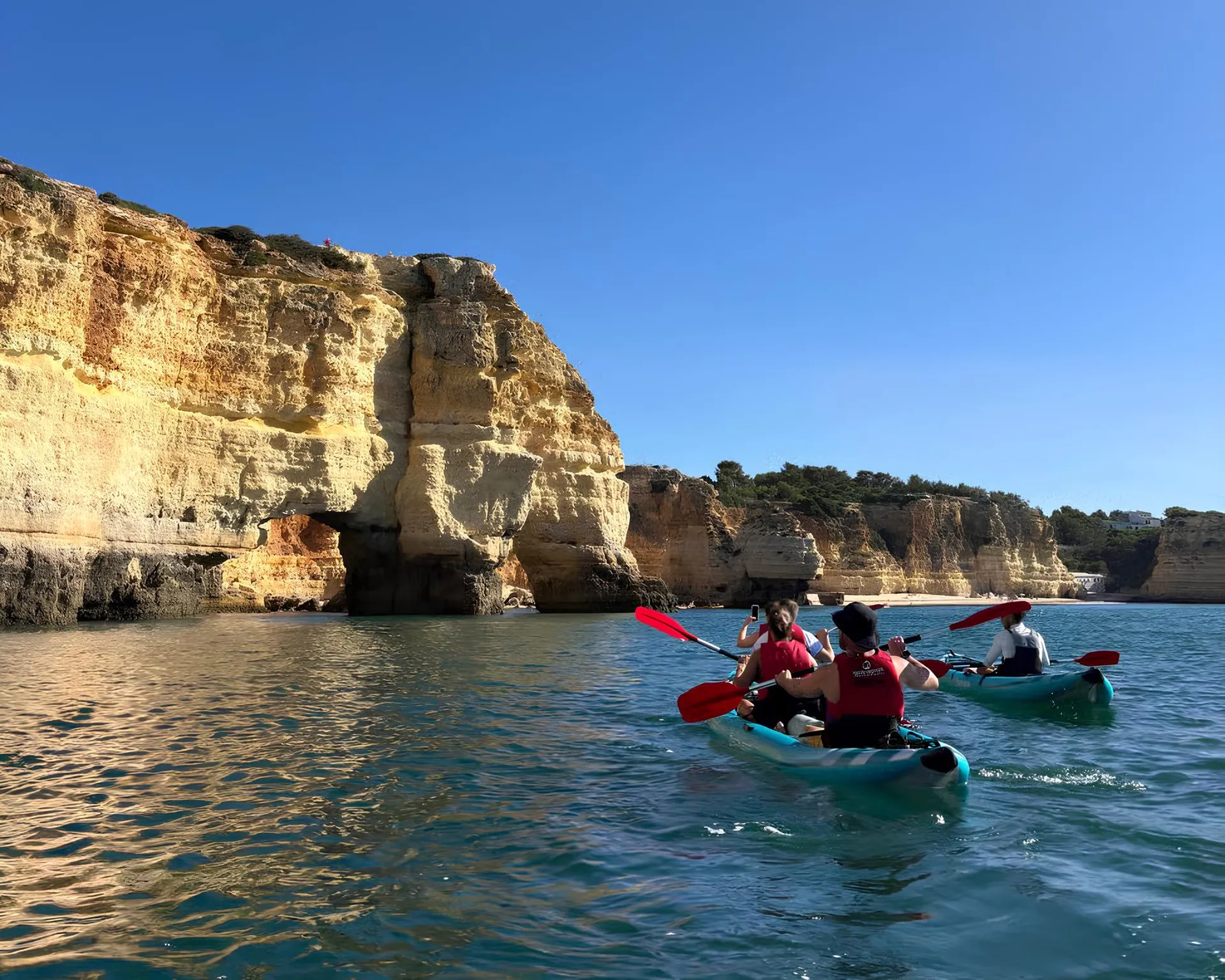 Couple kayaking along the golden limestone cliffs of Benagil, Algarve – calm turquoise sea with dramatic cliff faces in the background