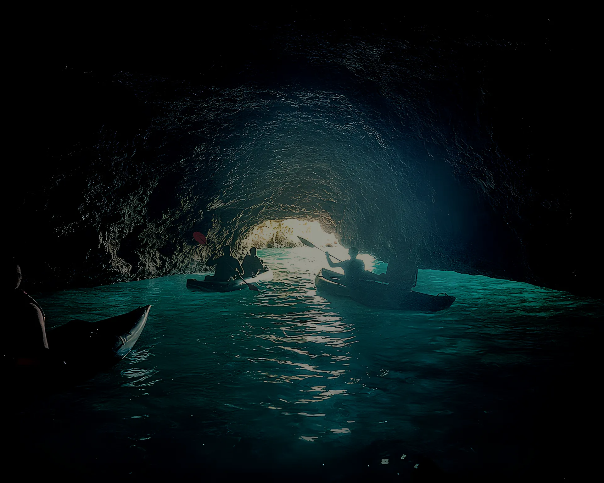 Silhouettes of kayakers inside the dark Pirate Cave near Benagil with turquoise water glowing at the cave entrance – Algarve sea cave tour