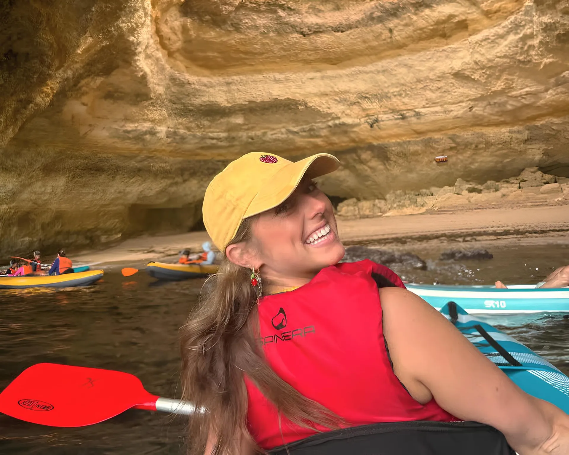 Happy guest smiling broadly from their kayak inside the Benagil Cave with the golden cave walls visible behind them
