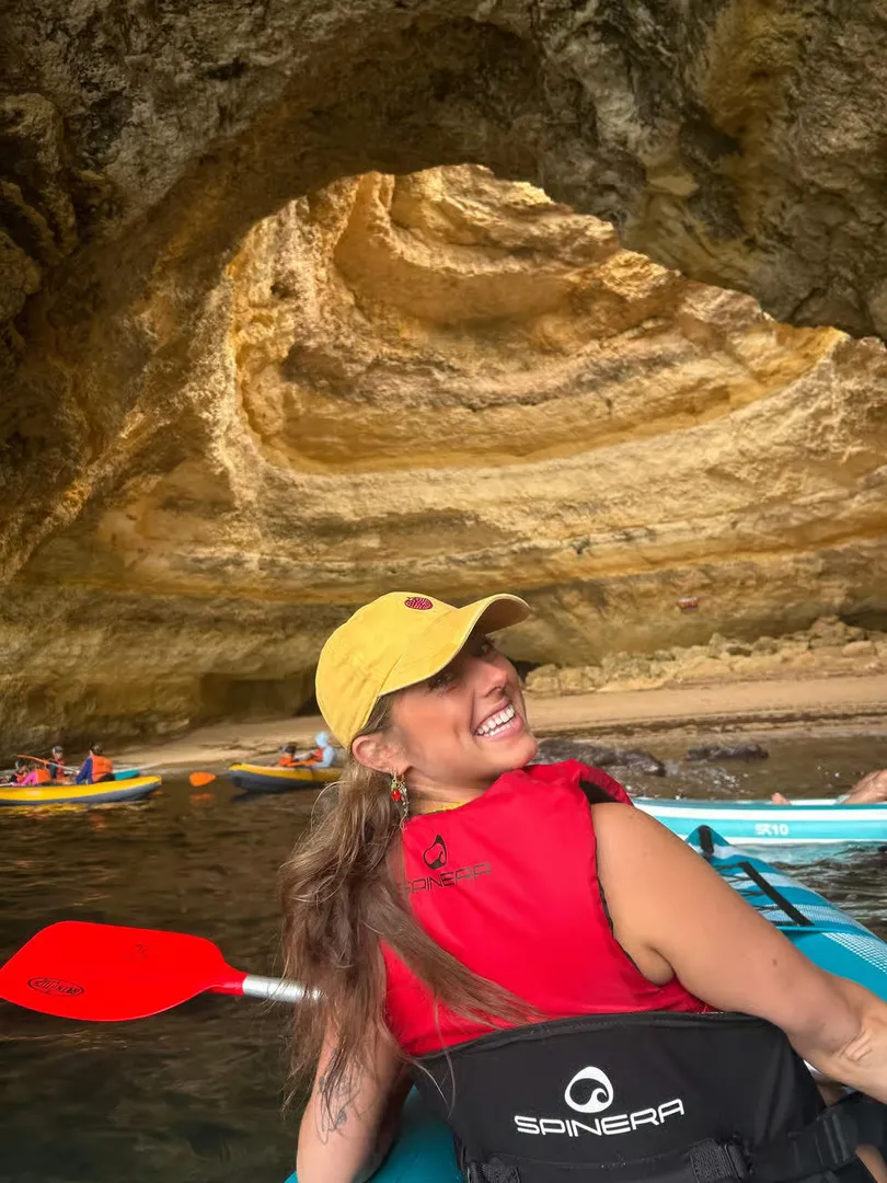 Portrait of a happy guest smiling from their kayak inside Benagil Cave – the cave skylight illuminates the background