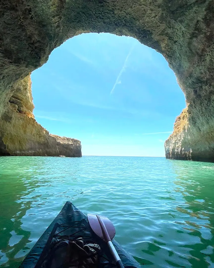 First-person view from a kayak approaching a sea arch along the Algarve coast, with clear water and golden rock formations