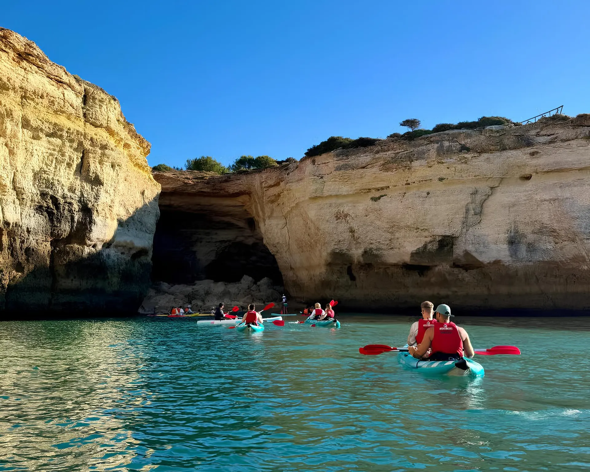 Kayak tour group approaching the entrance of a large sea cave along the Algarve coastline – golden cliffs frame the dark cave opening