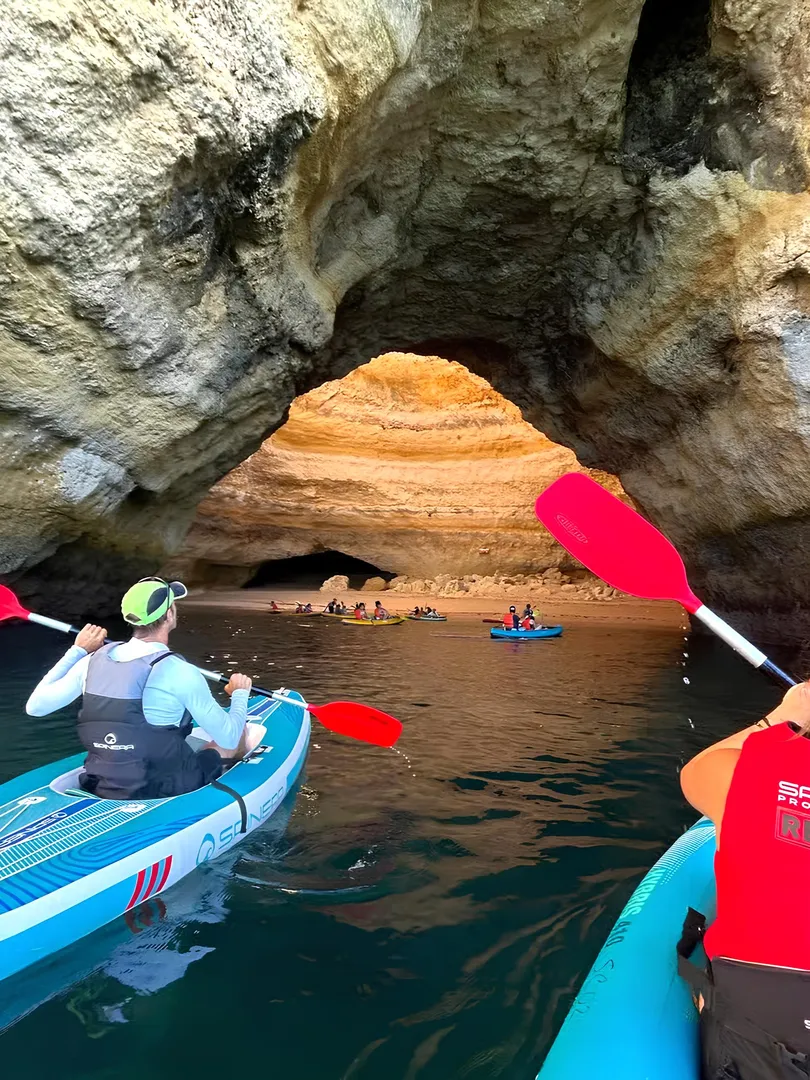 Kayaker passing through a rock arch revealing a hidden beach on the Algarve coast – accessible only by water