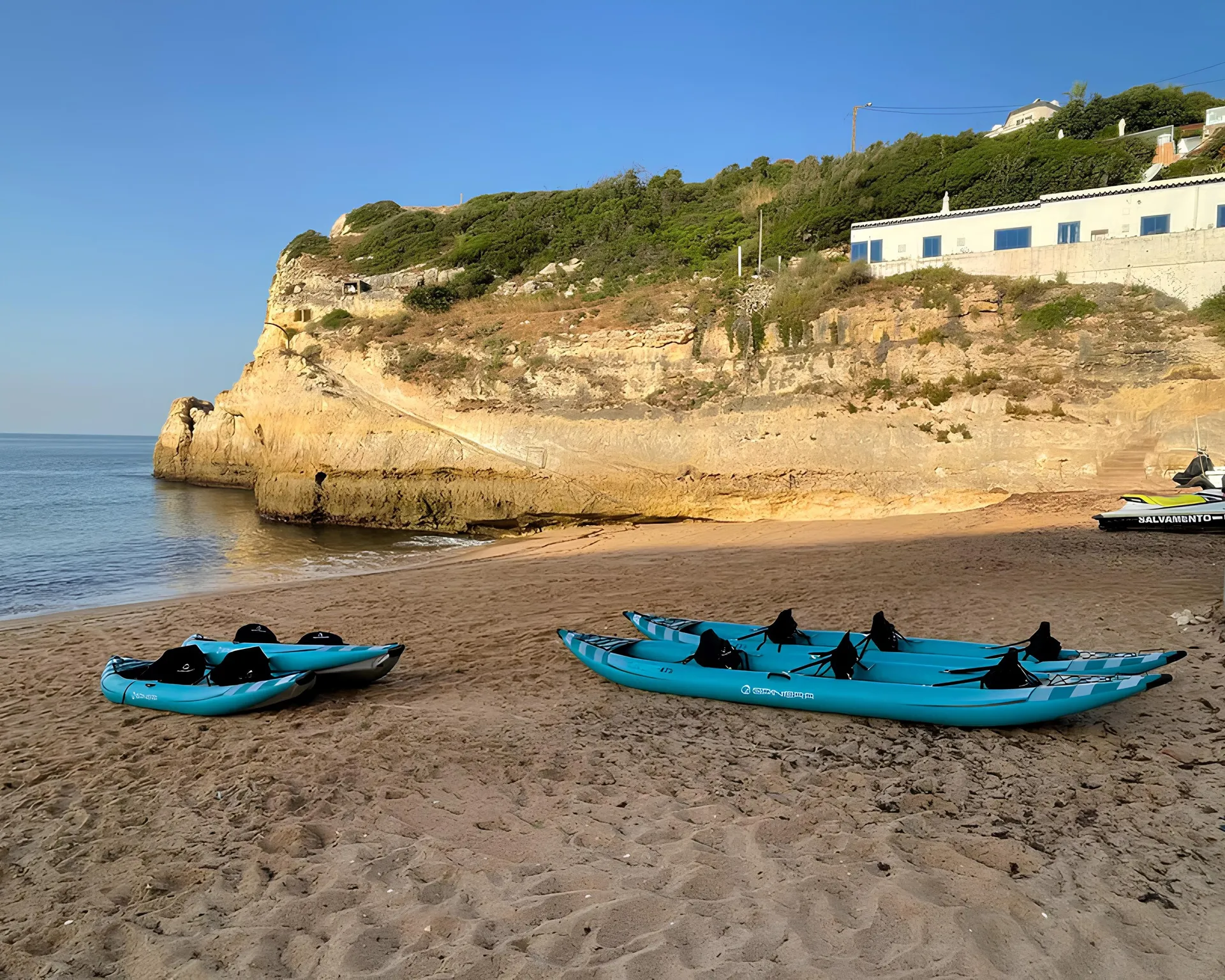 Colourful kayaks lined up on Benagil Beach ready for a Salty Cliffs guided tour – golden sand, blue sky, and Algarve cliffs in the background