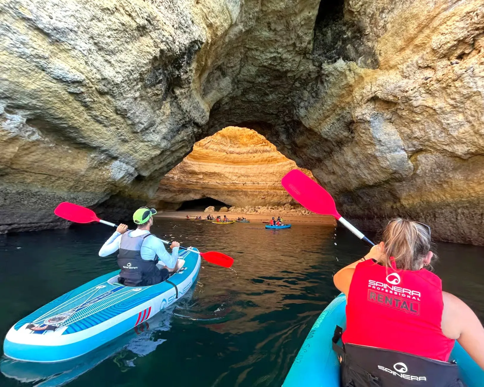 Kayakers paddling through a natural rock arch near Benagil Beach, Algarve – limestone formation frames the emerald sea beyond