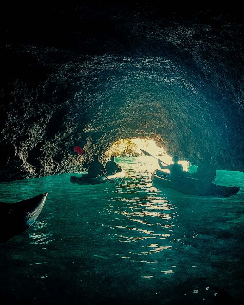 Dramatic silhouette of kayakers inside a dark sea cave with bright light streaming in from the entrance – Algarve kayak adventure