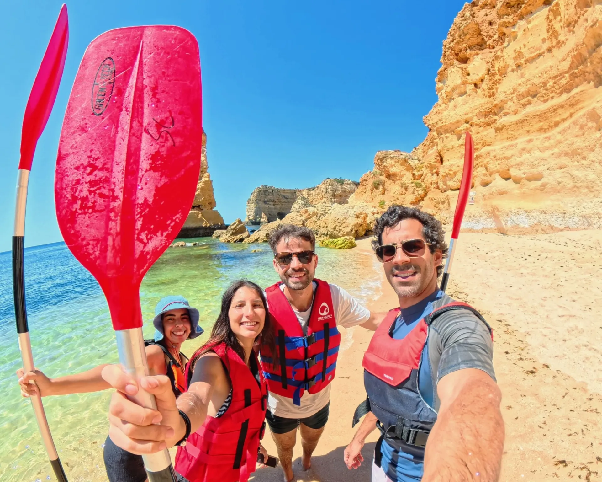 Salty Cliffs tour group selfie on Benagil Beach holding paddles up after completing a kayak tour – smiling guests in life jackets